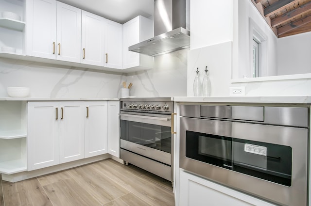 kitchen featuring high end stove, white cabinetry, oven, light wood-type flooring, and wall chimney exhaust hood