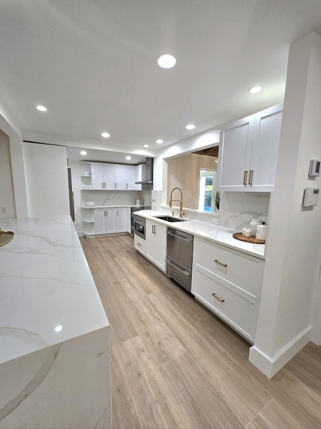 kitchen with sink, white cabinets, stainless steel dishwasher, light hardwood / wood-style floors, and wall chimney exhaust hood