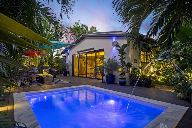 pool at dusk with a wooden deck and pool water feature