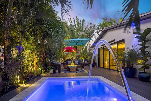 pool at dusk with an outdoor living space and a deck