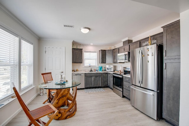 kitchen with dark brown cabinets, appliances with stainless steel finishes, ornamental molding, and visible vents