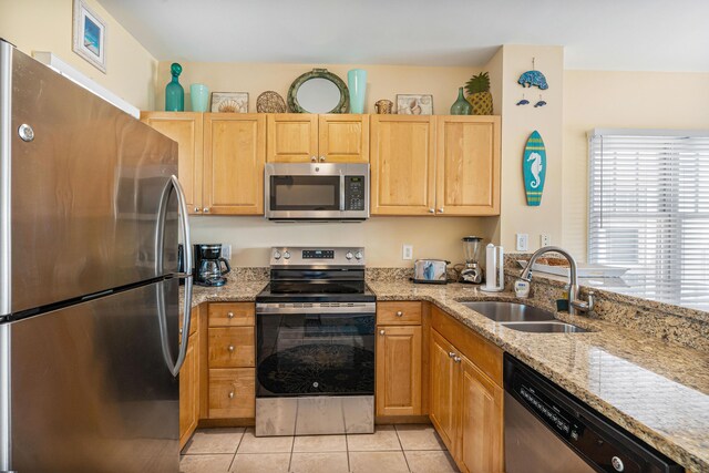 kitchen with light tile patterned floors, stainless steel appliances, a sink, and light stone countertops