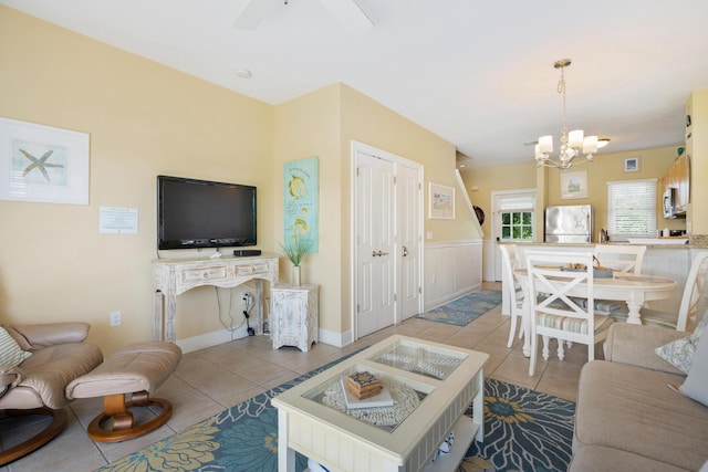 living room featuring wainscoting, light tile patterned flooring, and ceiling fan with notable chandelier