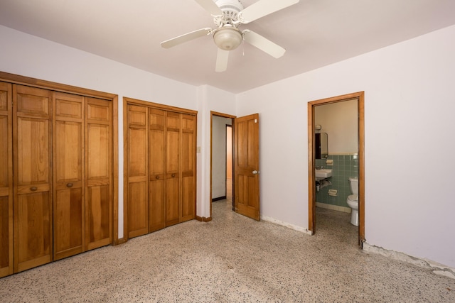 unfurnished bedroom with multiple closets, ceiling fan, tile walls, and ensuite bath