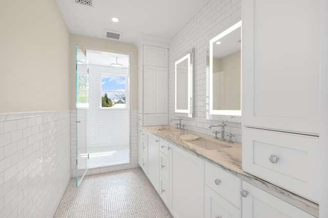 bathroom with double vanity, visible vents, tile walls, and a sink