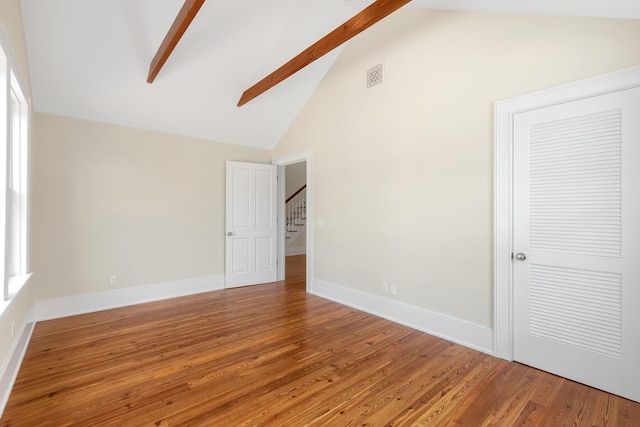 empty room featuring beam ceiling, visible vents, wood finished floors, high vaulted ceiling, and baseboards