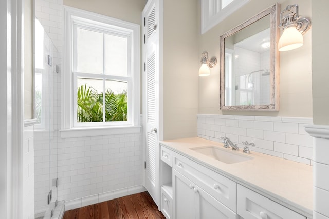 bathroom with wood finished floors, a shower stall, vanity, and tile walls