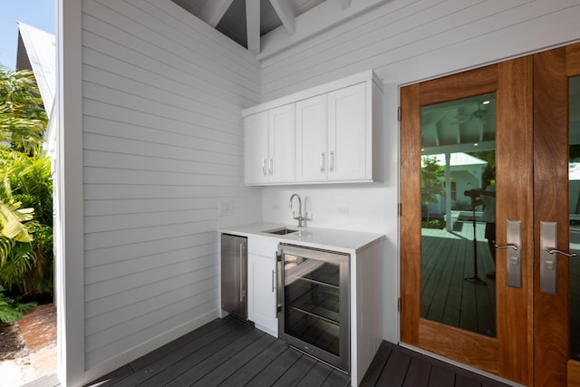 bar with beverage cooler, a sink, wood walls, and dark wood-style flooring