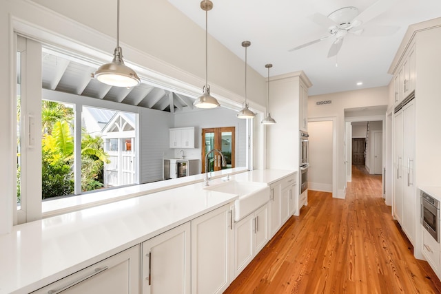 kitchen with light wood finished floors, light countertops, white cabinetry, pendant lighting, and a sink