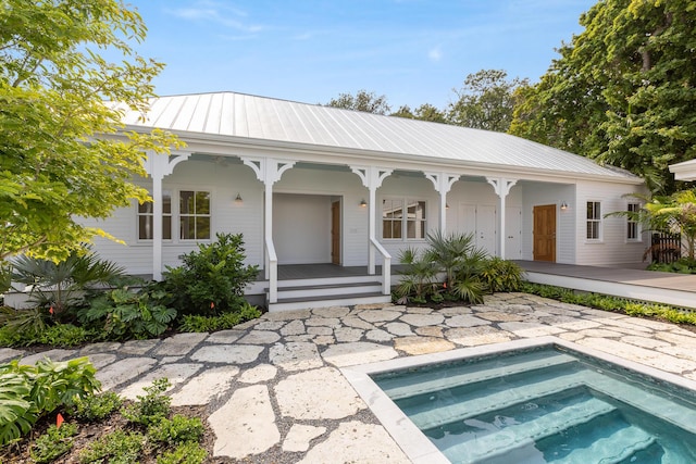 back of house featuring covered porch, metal roof, and an in ground hot tub