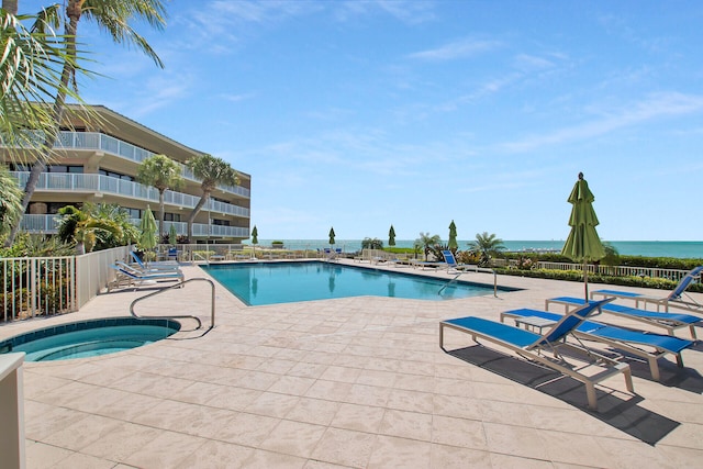 pool with a patio, a water view, fence, and a hot tub