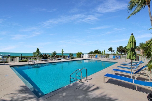 pool featuring a patio, a water view, and fence