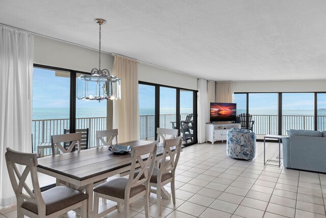 dining area with a chandelier, a water view, a textured ceiling, and light tile patterned flooring