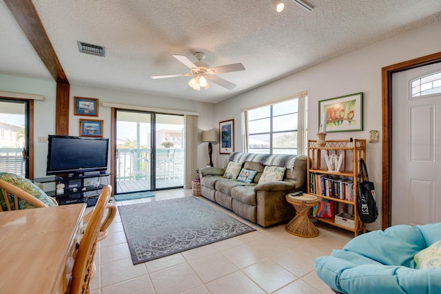 living room featuring a ceiling fan, visible vents, a textured ceiling, and light tile patterned floors