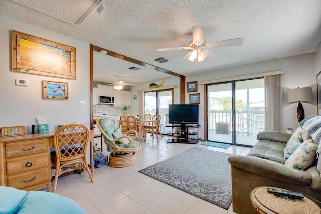 living room featuring light tile patterned floors, a textured ceiling, visible vents, and a ceiling fan