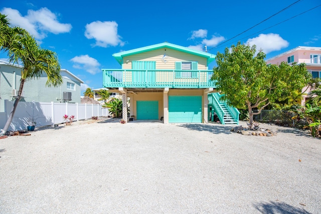 coastal inspired home with gravel driveway, an attached garage, stairs, and fence