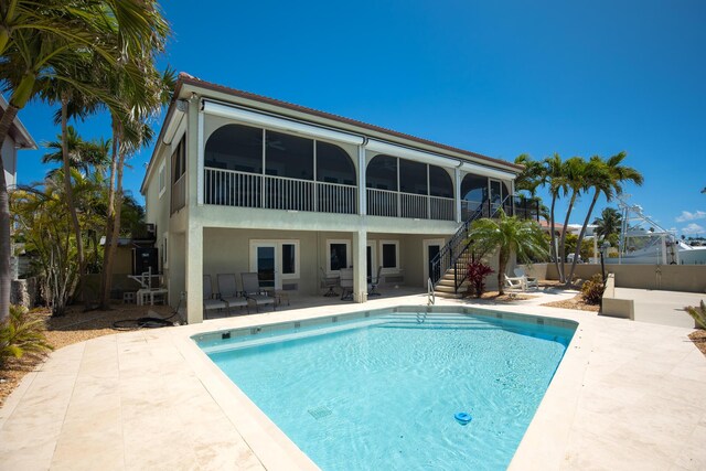 rear view of property featuring a sunroom, a patio, stairway, a fenced in pool, and a fenced backyard