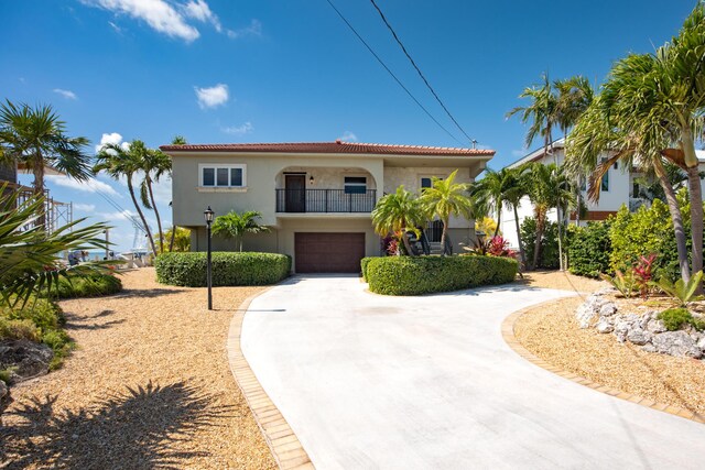 mediterranean / spanish-style home with a tile roof, a balcony, stucco siding, an attached garage, and curved driveway