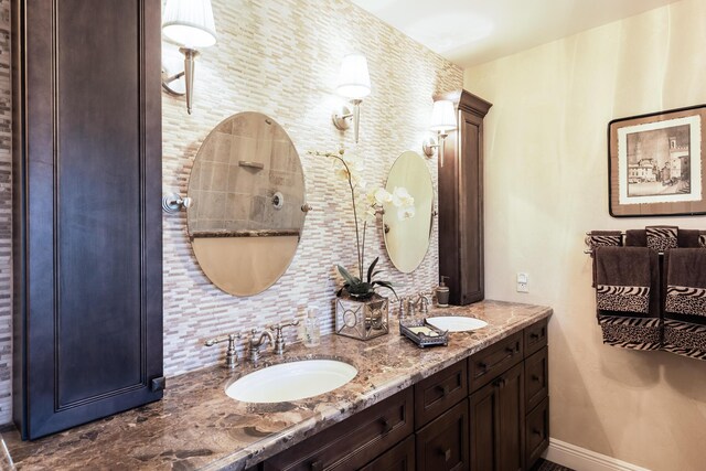 bathroom featuring baseboards, tasteful backsplash, double vanity, and a sink