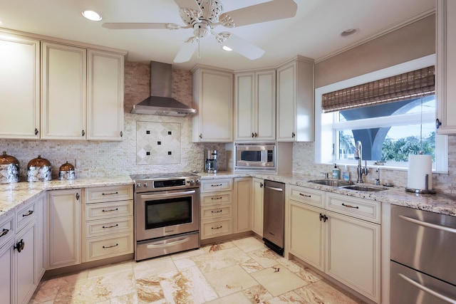 kitchen featuring stainless steel appliances, wall chimney exhaust hood, cream cabinets, and a sink