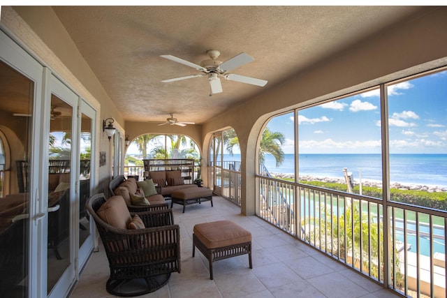 sunroom featuring a water view, tile patterned floors, outdoor lounge area, a ceiling fan, and a textured ceiling