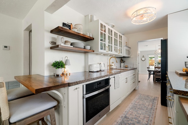 125 Harbor Dr, Key Largo, FL 33037 - kitchen with stainless steel oven, glass insert cabinets, white cabinetry, open shelves, and light wood-style floors