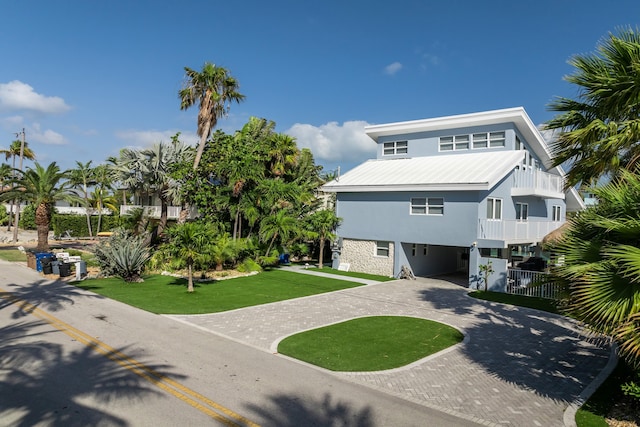 coastal home with a front yard, decorative driveway, stucco siding, metal roof, and a carport