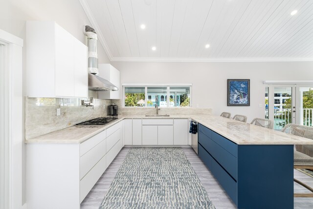 kitchen with a peninsula, stainless steel gas cooktop, modern cabinets, wall chimney range hood, and a kitchen bar