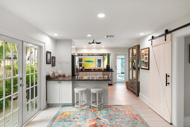 kitchen featuring appliances with stainless steel finishes, white cabinets, kitchen peninsula, a barn door, and french doors