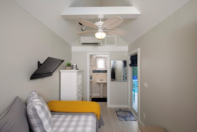 bedroom with lofted ceiling, a wall mounted air conditioner, connected bathroom, and light hardwood / wood-style flooring