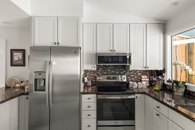 kitchen with lofted ceiling, white cabinetry, tasteful backsplash, dark stone counters, and stainless steel appliances