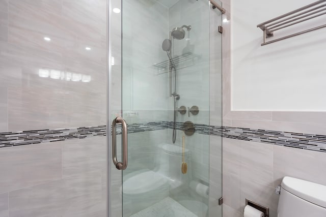 bathroom with tile walls, an enclosed shower, and toilet