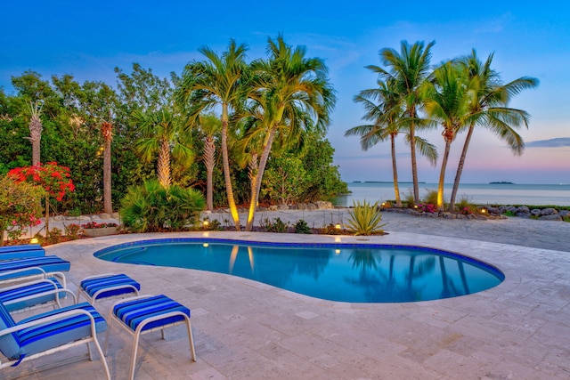 pool at dusk featuring a water view, a patio area, and an outdoor pool