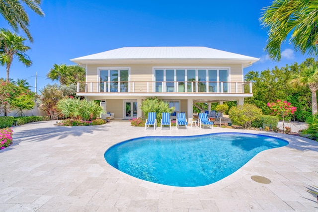 back of property with an outdoor pool, french doors, a patio, and a balcony