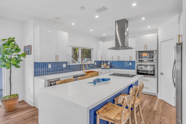 kitchen featuring island range hood, stainless steel appliances, light countertops, a kitchen bar, and white cabinetry