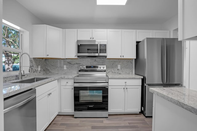 kitchen with appliances with stainless steel finishes, light stone countertops, sink, and white cabinets