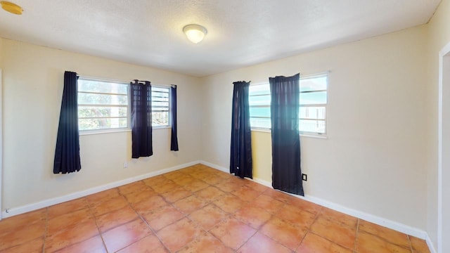 tiled empty room with plenty of natural light and a textured ceiling