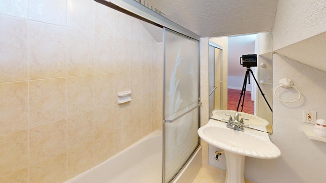 bathroom featuring a textured ceiling and combined bath / shower with glass door