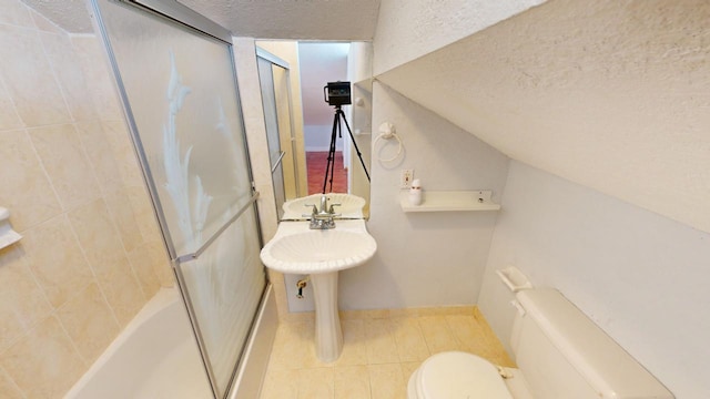 bathroom with tile patterned flooring, combined bath / shower with glass door, a textured ceiling, and toilet