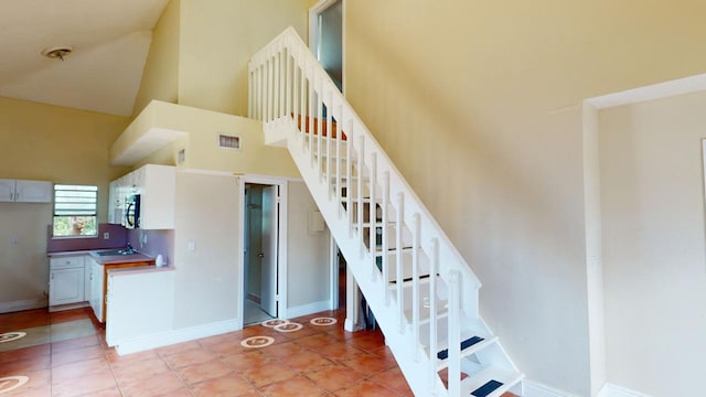 staircase with sink, tile patterned flooring, and high vaulted ceiling