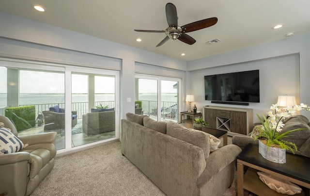 living room featuring a water view, ceiling fan, and light carpet