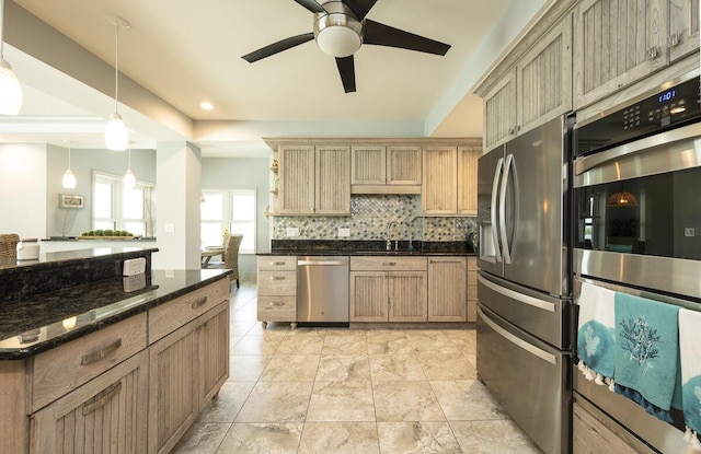 kitchen featuring sink, dark stone countertops, stainless steel appliances, tasteful backsplash, and decorative light fixtures