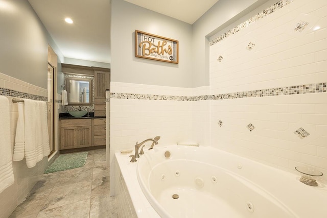 bathroom featuring vanity, tiled bath, and tile walls