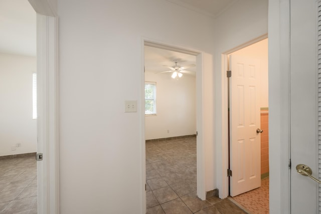 hall featuring crown molding, baseboards, and tile patterned flooring