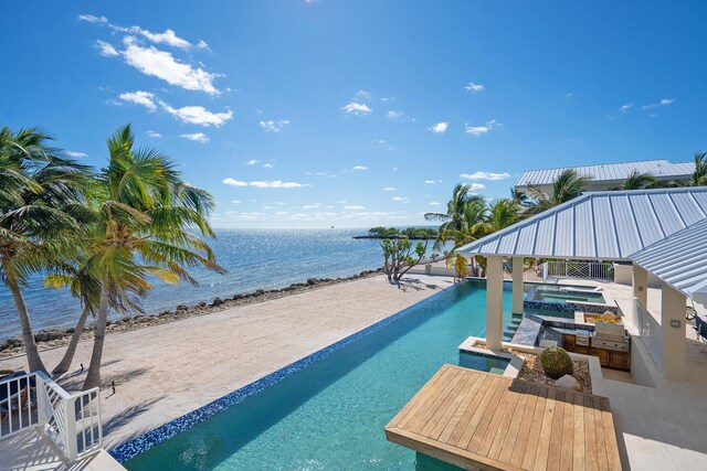 view of pool with a view of the beach, an outdoor kitchen, a patio, and a water view