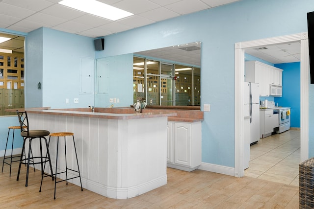 bar featuring white appliances, a drop ceiling, light hardwood / wood-style flooring, and white cabinets