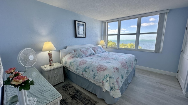 bedroom with a water view, light wood-type flooring, and a textured ceiling