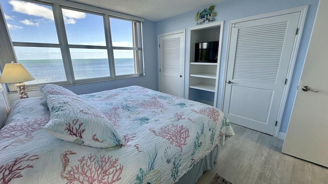 bedroom with multiple closets, a textured ceiling, and light wood-type flooring