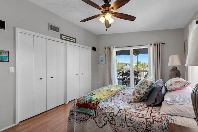 bedroom featuring wood-type flooring, a textured ceiling, access to outside, multiple closets, and ceiling fan