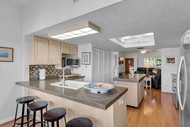 kitchen with tasteful backsplash, light wood-type flooring, appliances with stainless steel finishes, a kitchen breakfast bar, and kitchen peninsula